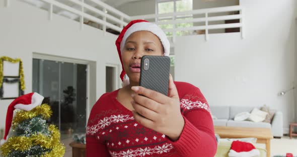 Happy african american plus size woman in santa hat, making video call on smartphone at christmas