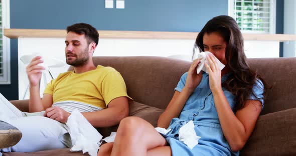 Couple blowing their nose in tissue in living room at home