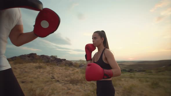 Woman Trains Her Punches on Her Paws Together with a Trainer in Nature Against the Sky Bottom View