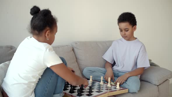 African American Brother and Sister Playing Chess on Couch at Living Room