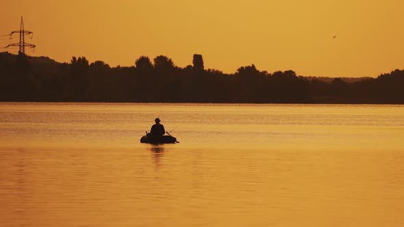 Boat with a fisherman in the sunset light floats slowly on the lake.