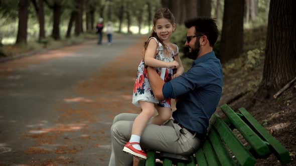 Daughter With Father Sitting On Bench. Happy Beautiful Family Relaxing Together In Park.