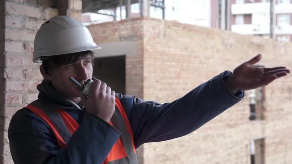 A construction engineer at a construction site controls a crane using a radio walkie-talkie.