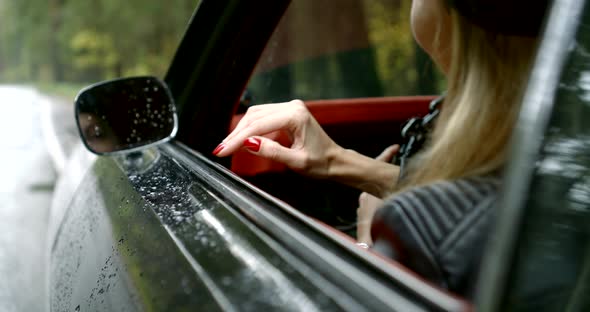 Woman Is Sitting in Luxury Car Parked on Roadside in Rainy Day, Smiling, View on Face in Rear Mirror