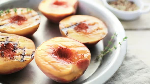 Organic grilled peaches with fresh thyme on a metal plate.