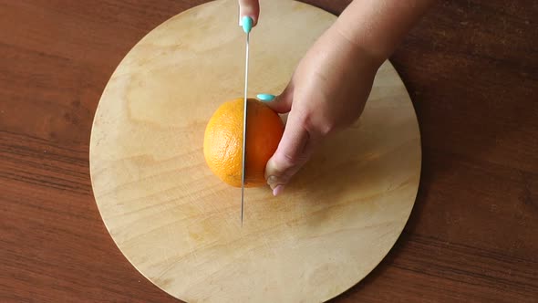 Closeup of a Woman Cutting a Ripe Juicy Orange with a Knife