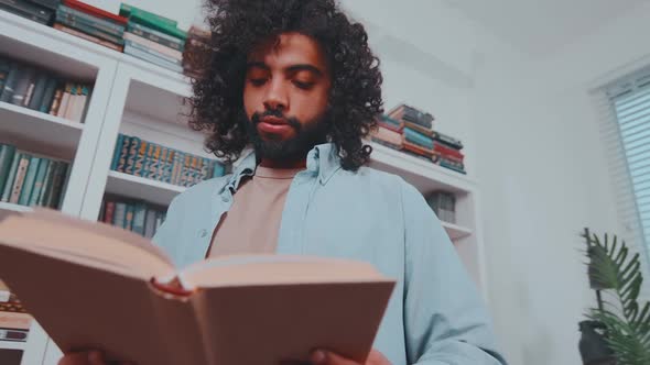 Young Focused Middle Eastern Man Reads and Flips Through Book Stands in Library