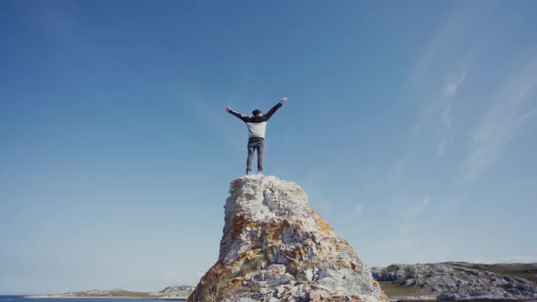 Traveler on high rock under blue sky