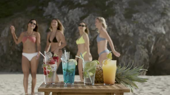 Cold Refreshing Cocktails on Table and Girls Dancing on Beach