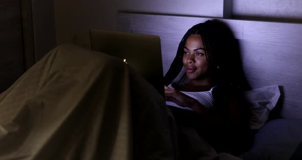 Black Woman using laptop in bed at home.