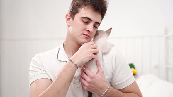 a Young Man Holds a Small White Kitten and Petting Him