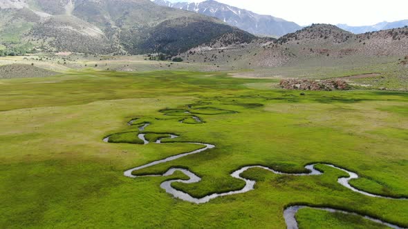 Aerial View of Green Land and Small Curve River with Mountain in the Background in Aspen Springs