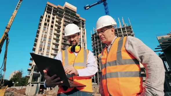 Two Men Work with a Laptop on a Building Site. alt