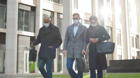 Group of Colleagues in Formal Suit and Safety Mask Walking Together Past City Building Outdoors
