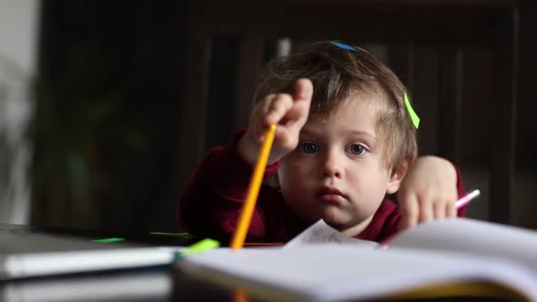 Little boy play with notebook, stickers and parents laptop at table at home