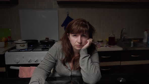 Boring Woman Sitting in the Kitchen in the Evening and Looking at the Camera