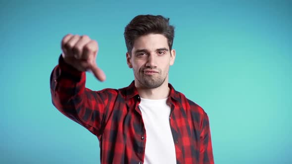 Young Handsome Man Standing on Blue Studio Background Showing Thumb Down Gesture