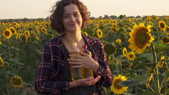 Portrait Of Brunette Woman Holding Bottles Of Sunflower Oil, Standing Against Flowers Of Sunflower