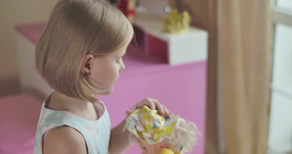 Side View Close-up of Caucasian Girl's Face Looking at Camera and Signing As Playing with Her Doll