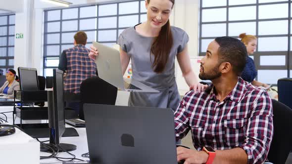 Business executives interacting while using laptop