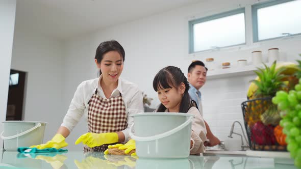 Asian young family teaching their little girl daughter to clean dining table in house with happiness