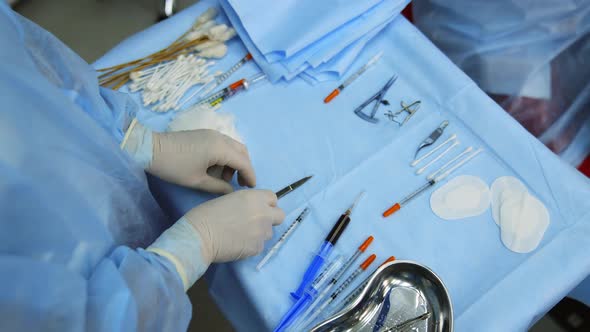 Medic chooses surgical instruments. Scalpel and scissors and syringes and needles and clamps. 