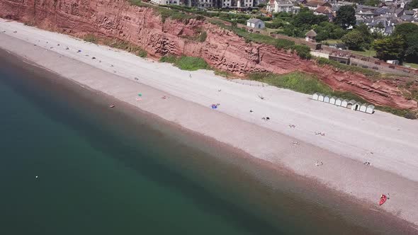 Aerial view of coarse Triassic cliffs, pebble beach with sunbathing people, sea and beachfront build