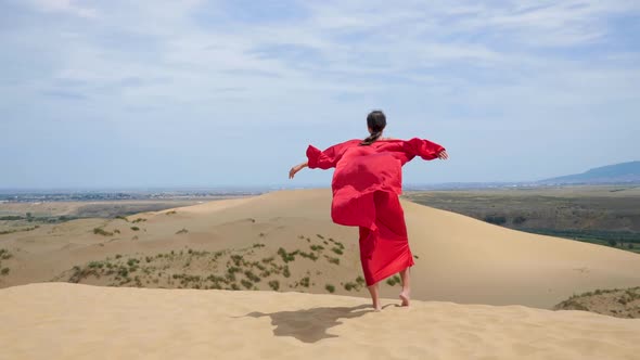 Sexy Brunette Woman in a Red Satin Long Dress Walks on Sand Dunes in the Desert
