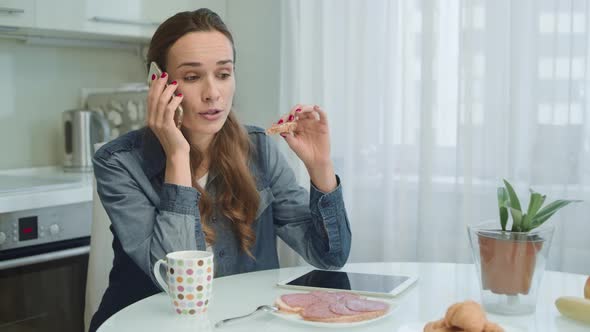 Woman Talking on Phone While Eating Breakfast. Girl Eating Tasty Sandwich