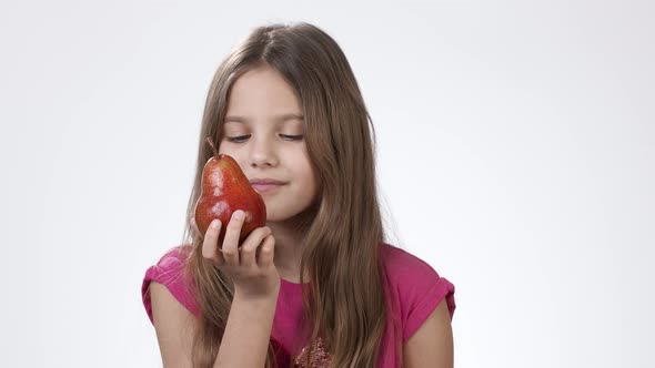 A Little Girl on a White Background Holds in His Hand a Ripe Fragrant Pear. The Girl Bites and Eats