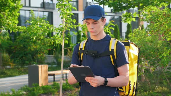 Delivery Man Courier with Thermal Backpack Uses Tablet Confirm Client Order