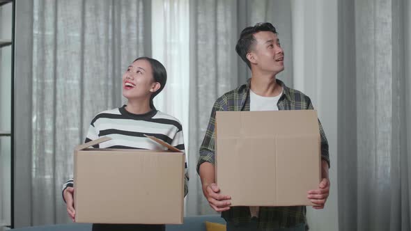 Smiling Young Asian Couple Carrying Cardboard Boxes With Stuff Into A New House Then Looking Around