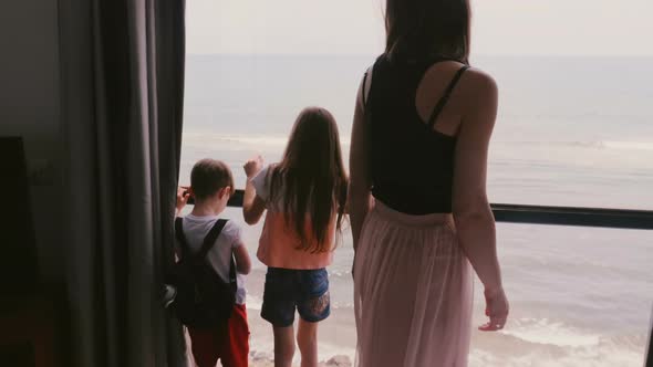 Young Mother with Two Happy Excited Little Kids Together at Large Apartment Window Watching 
