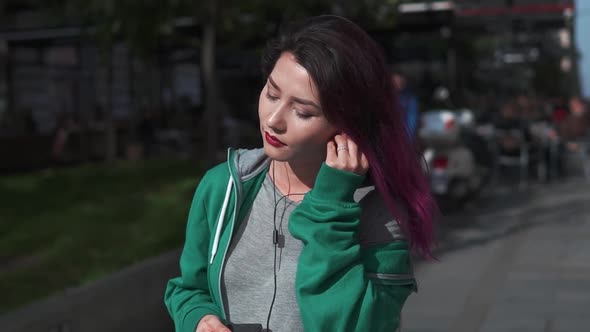 Attractive Young Woman with Colored Hair Enjoying Music in Earphone Using Smartphone and Walk