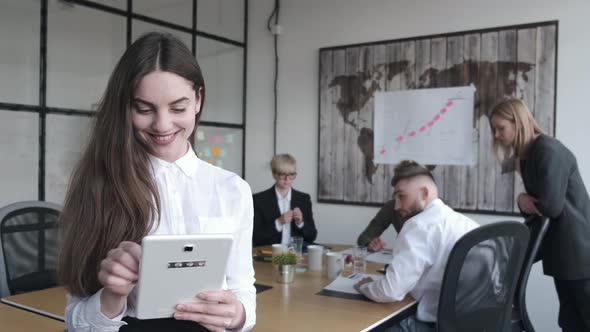 The Woman Is Standing with a Tablet in the Office with Collegues