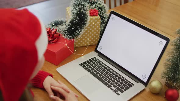 Caucasian woman wearing santa hat making video call at home on laptop with copy space on screen