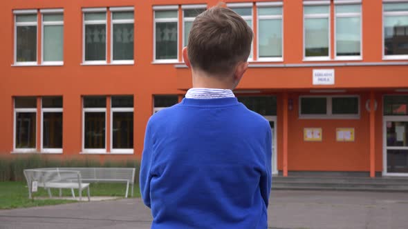 A Young Boy Stands in Front of an Elementary School and Looks Around