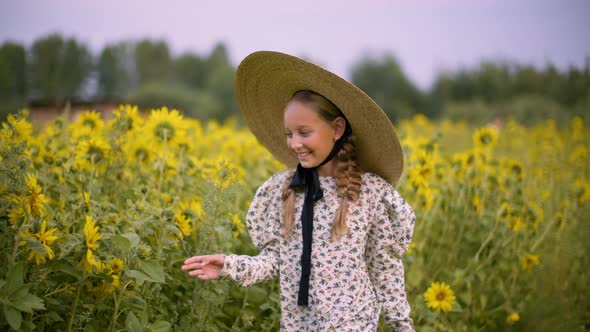 Smiling Teenager Girl in Hat Touching Sunflowers on Summer Walk at Rustic Field. Happy Young Girl