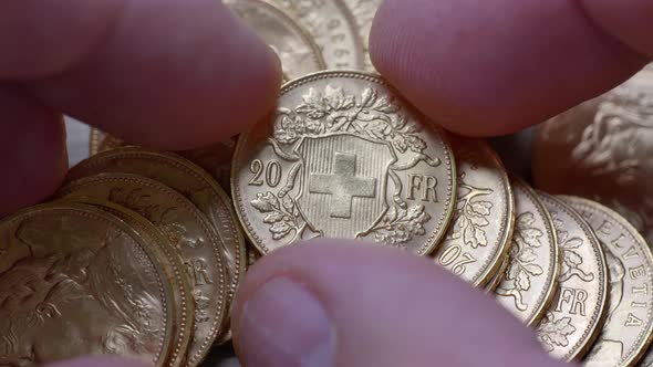 Male hand surveying bunch of golden twenty franc coins lighting in studio,close up shot.