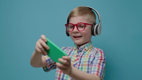 Preschool Boy Playing Video Game on Mobile Phone and Showing Thumb Up Looking at Camera