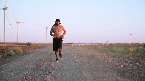 A muscular, athletic Arab man with a beard running in a field against the backdrop of windmills.