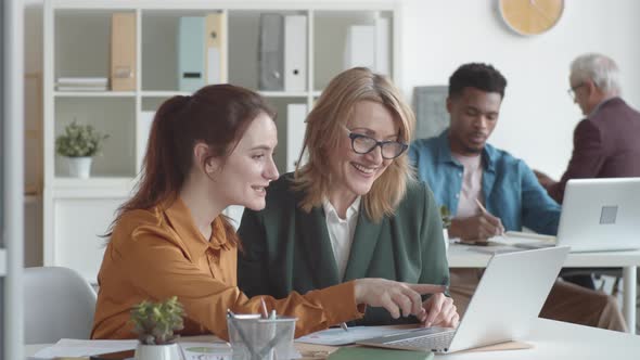 Young Caucasian Woman and Senior Female Colleague Looking at Laptop Screen