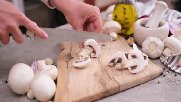 Woman Cuts Champignon Mushrooms with a Knife on a Wooden Cutting Board