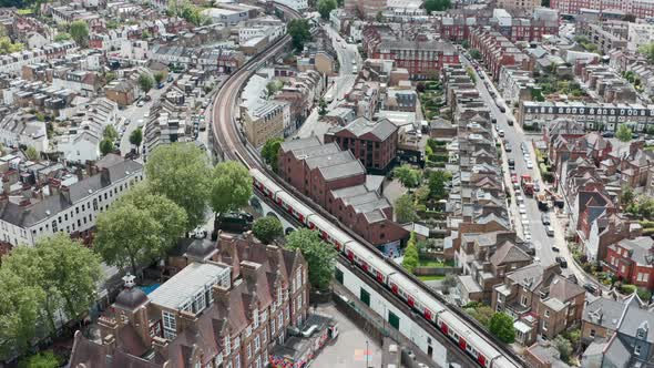 Cinematic drone follow shot of district line train winding through residential London Putney bridge