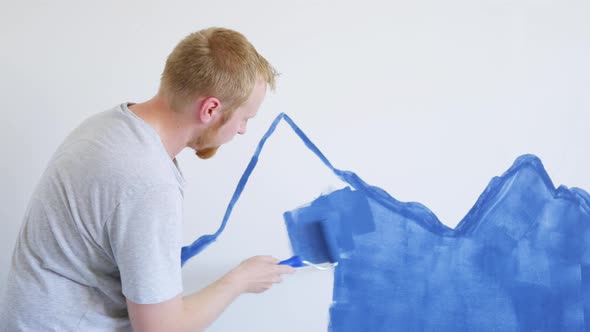 a man paints a wall in a room, draws blue mountains in a nursery