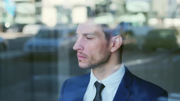 Worried businessman looking through window pane reflecting city life