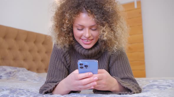 Happy woman using social media app in smartphone while lying in bedroom in 4k stock video