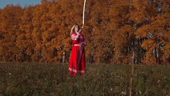 Militant Concept on an Autumn Field - Feisty Blonde Woman in Red National Dress Training Her