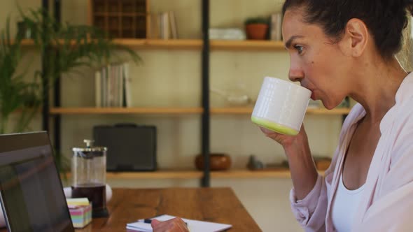 Mixed race woman drinking coffee and working from home