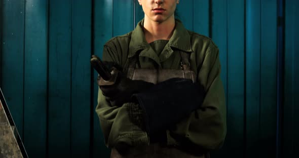 Female welder standing with arm crossed in workshop